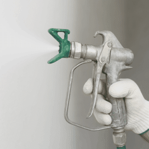 Main gantée tenant un pistolet à peinture professionnel gris, pulvérisant de la peinture blanche. Buse verte visible.