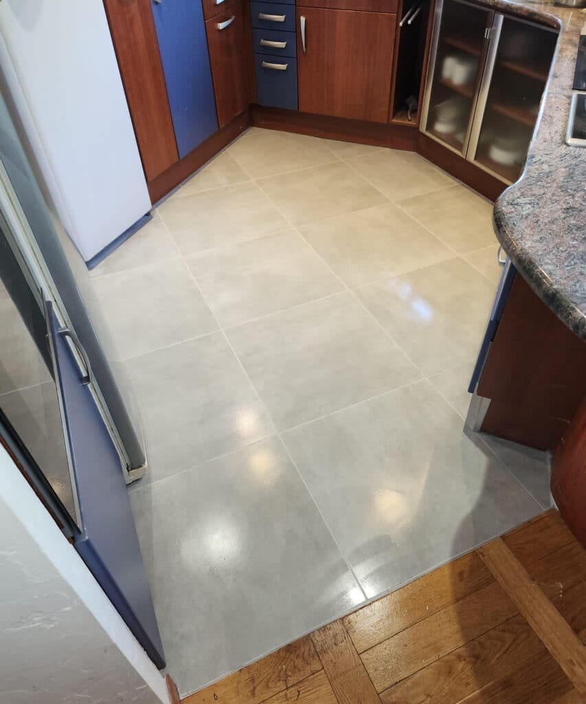 Carrelage de cuisine gris clair brillant posé entre des meubles en bois et un parquet naturel.