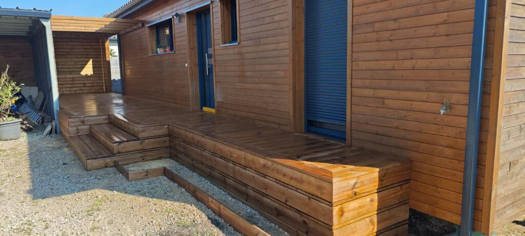 Terrasse et bardage en bois d'une maison moderne avec escaliers intégrés sur un sol en gravier.