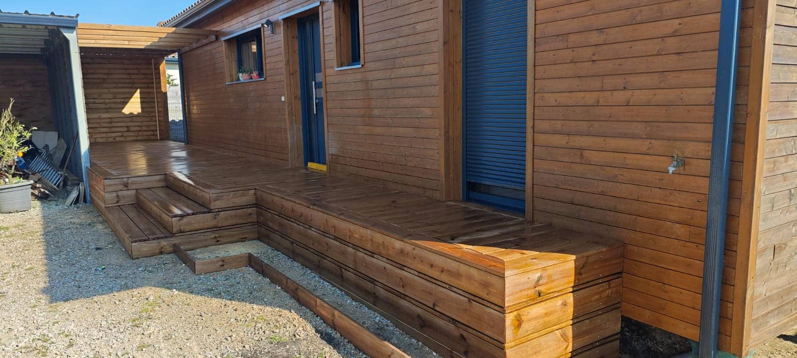 Terrasse et bardage en bois d'une maison moderne avec escaliers intégrés sur un sol en gravier.